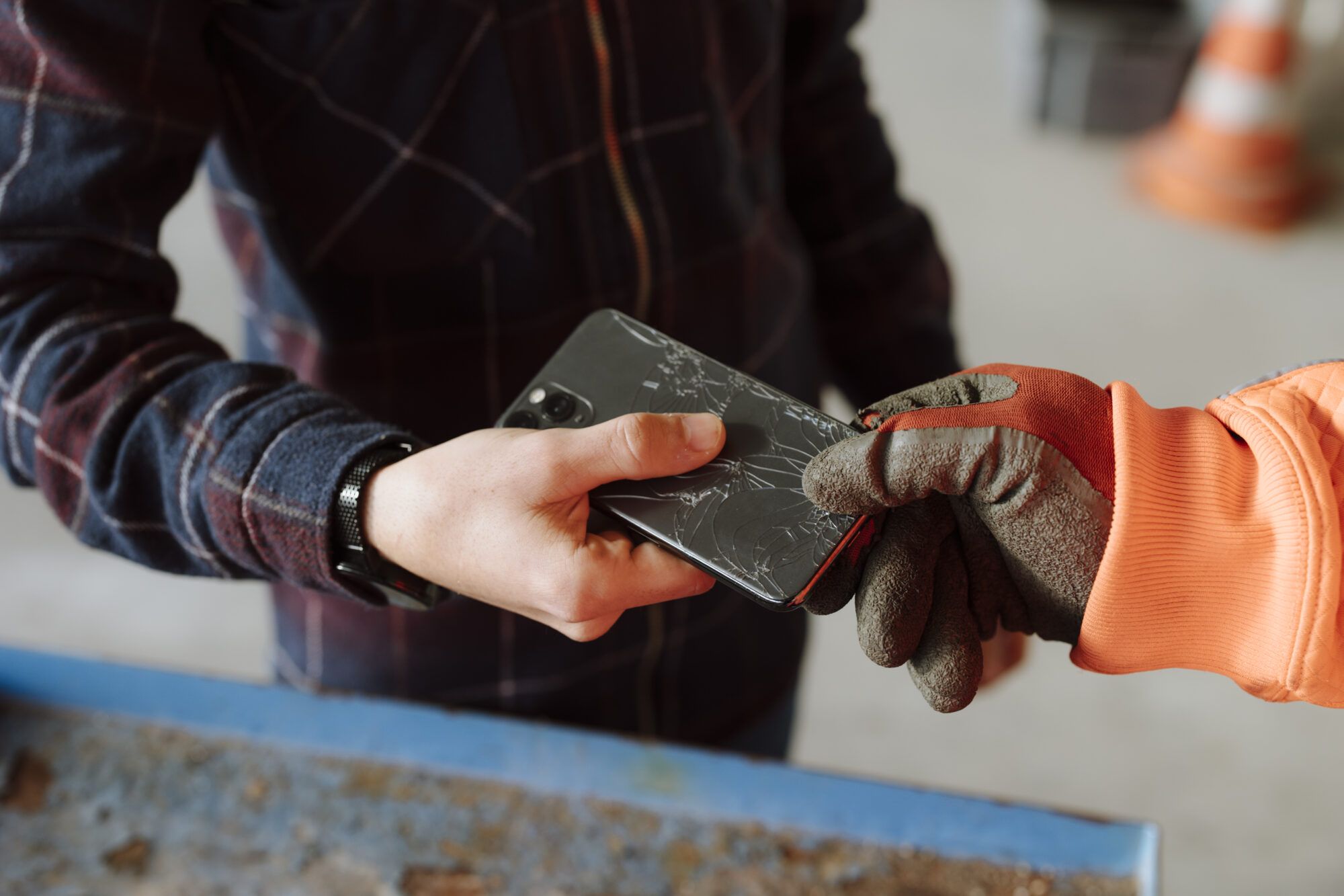 Man sieht den Ausschnitt einer M&auml;nnerhand, die ein defektes Handy einem WSZ-Mitarbeiterhand &uuml;bergibt. 